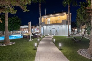 Ein modernes, zweistöckiges Haus mit Swimmingpool, Sitzgelegenheit im Freien und einem gut beleuchteten Weg.