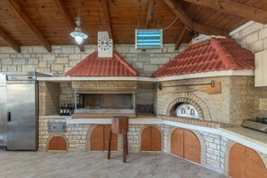 Une cuisine extérieure en pierre, dotée d’un four encastré, d’un réfrigérateur et d’un luminaire suspendu.