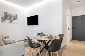 Ein modernes Wohnzimmer mit einem runden Esstisch, schwarzen Stühlen, einem grauen Sofa, einem Flachbildfernseher und einem großen Wandbild.