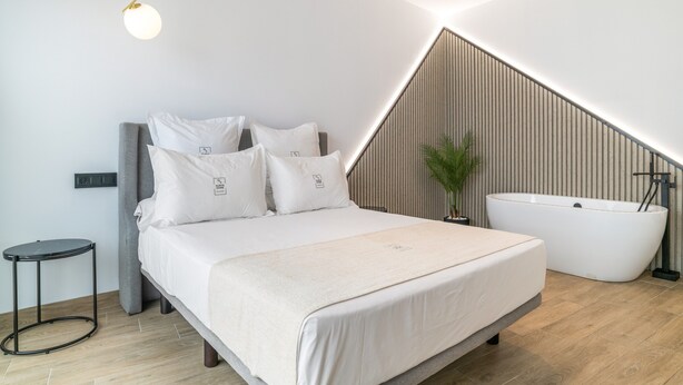 Quarto moderno com cama, mesa de cabeceira e banheira independente.