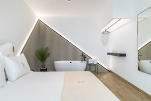 A modern bedroom with a large bed, a freestanding bathtub, a potted plant, a mirror, and a wooden floor. - Studio Apartment '103' with Wi-Fi and Air Conditioning (Conil de la Frontera)