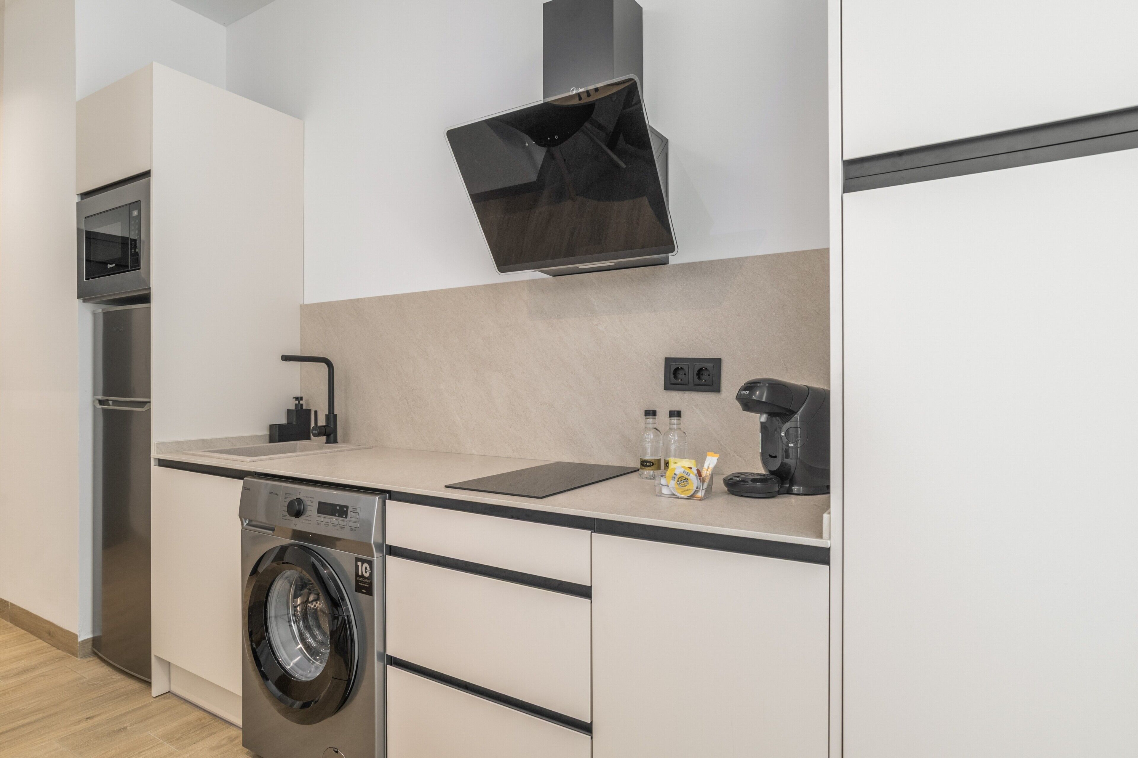 A modern kitchen with a built-in washing machine, a microwave, and a coffee machine.