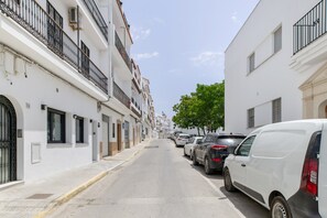 Eine schmale Straße gesäumt von weißen Gebäuden, parkenden Autos und einem Baum.
