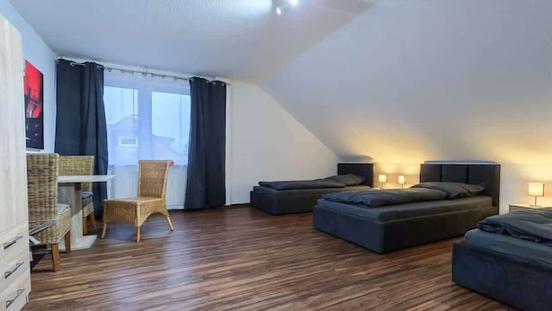A loft-style room with a sloped ceiling, a wooden floor, a bed, a chair, a desk, and a window with curtains. - Alpha Apartments: Grand Space | 6 Beds & Parking (Datteln)