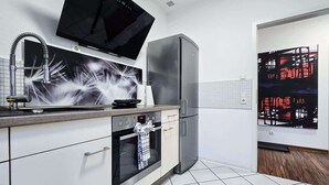 A modern kitchen with a built-in oven, a stainless steel refrigerator, and a flat-screen TV mounted above the oven. - Alpha Apartments: Grand Space | 6 Beds & Parking (Datteln)