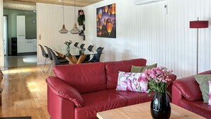 A red leather sofa with a vase of flowers, a wooden coffee table, and a dining area with a glass table and chairs. - 4 Star Holiday Home in Ans By (Ans)