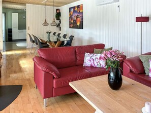Ein rotes Ledersofa mit Blumen in einer Vase, ein Holztisch und ein Essbereich mit einem Glastisch und Stühlen.