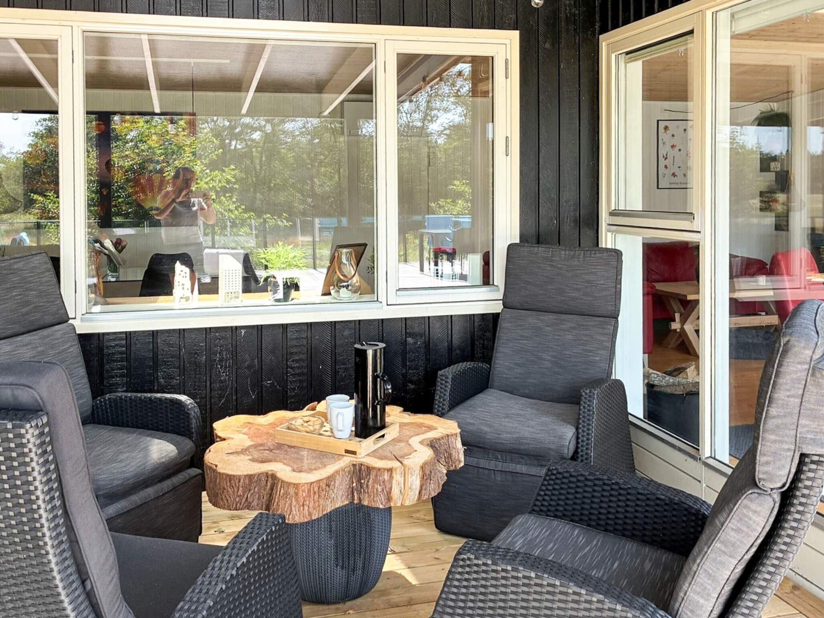 Un espace extérieur accueillant, aménagé avec des meubles en osier et une table basse en bois, doté de grandes fenêtres et offrant une vue sur l’extérieur.