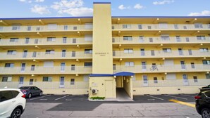 Un hotel de diverses plantes amb un eix central d'ascensor, balcons a cada planta i un aparcament ple de cotxes.