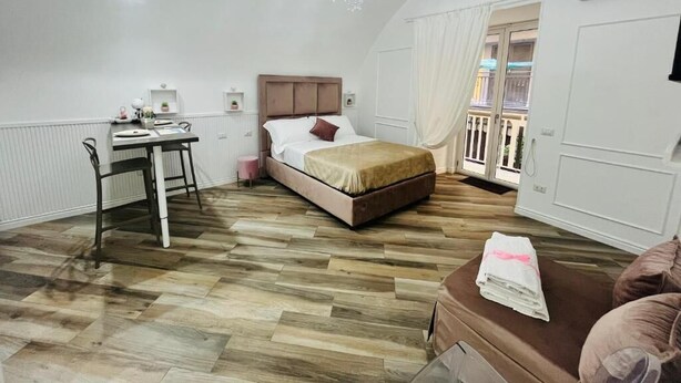 Un dormitorio con cama, escritorio, silla, candelabro y vista al balcón.