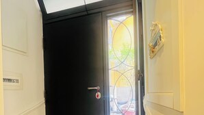 Una habitación con una puerta negra cerrada, un escalón pequeño que lleva a un balcón y una lámpara fijada a la pared.