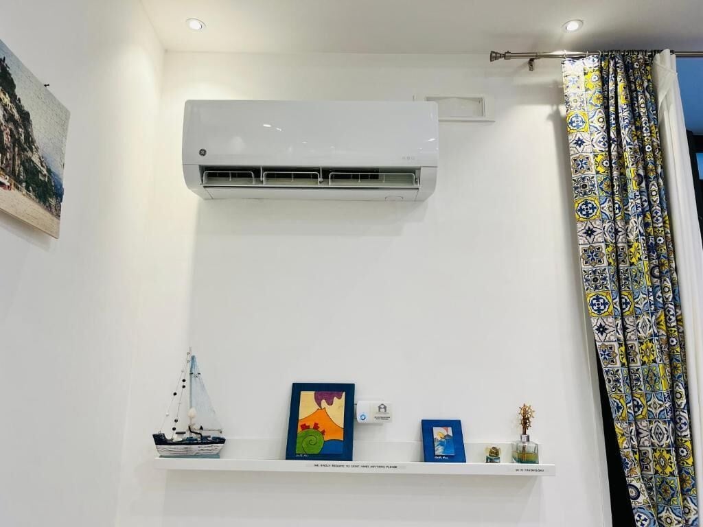 Une pièce avec un climatiseur blanc, une étagère ornée d’objets décoratifs et un rideau à motifs.