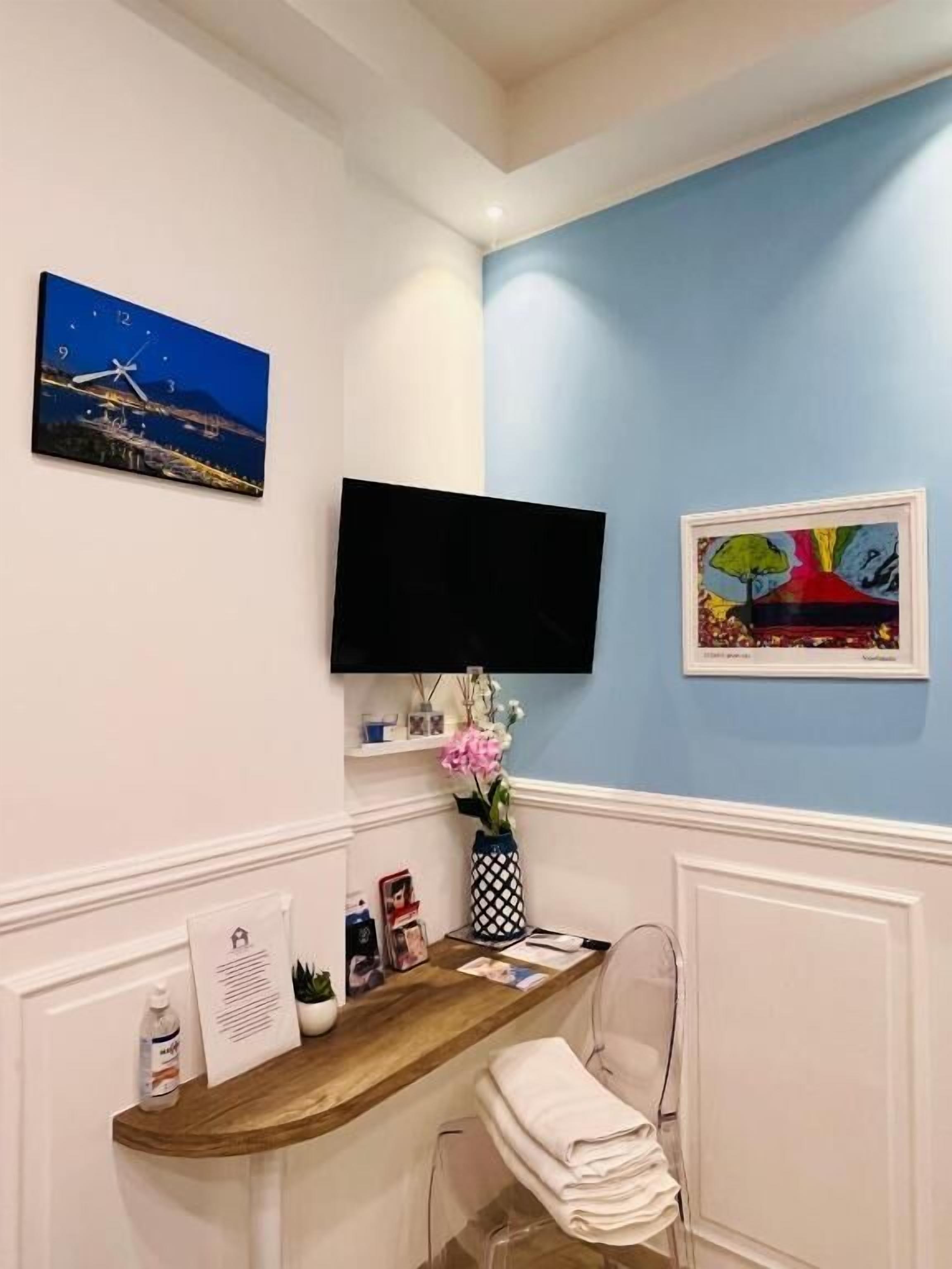 A room with a wooden desk, a flat-screen TV mounted on the wall, and two framed artworks.