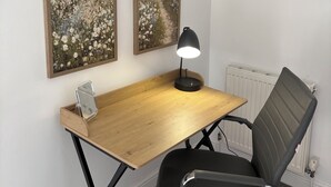 Ein Arbeitsplatz mit einem Holztisch, einem schwarzen Bürostuhl, einer Schreibtischlampe und zwei Landschaftsbildern an der Wand.