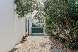 A narrow pathway leading to a gated entrance, flanked by potted plants and dense foliage. - Guéthary: Between the Ocean and the Village, Terraces, and Gardens (Guéthary)