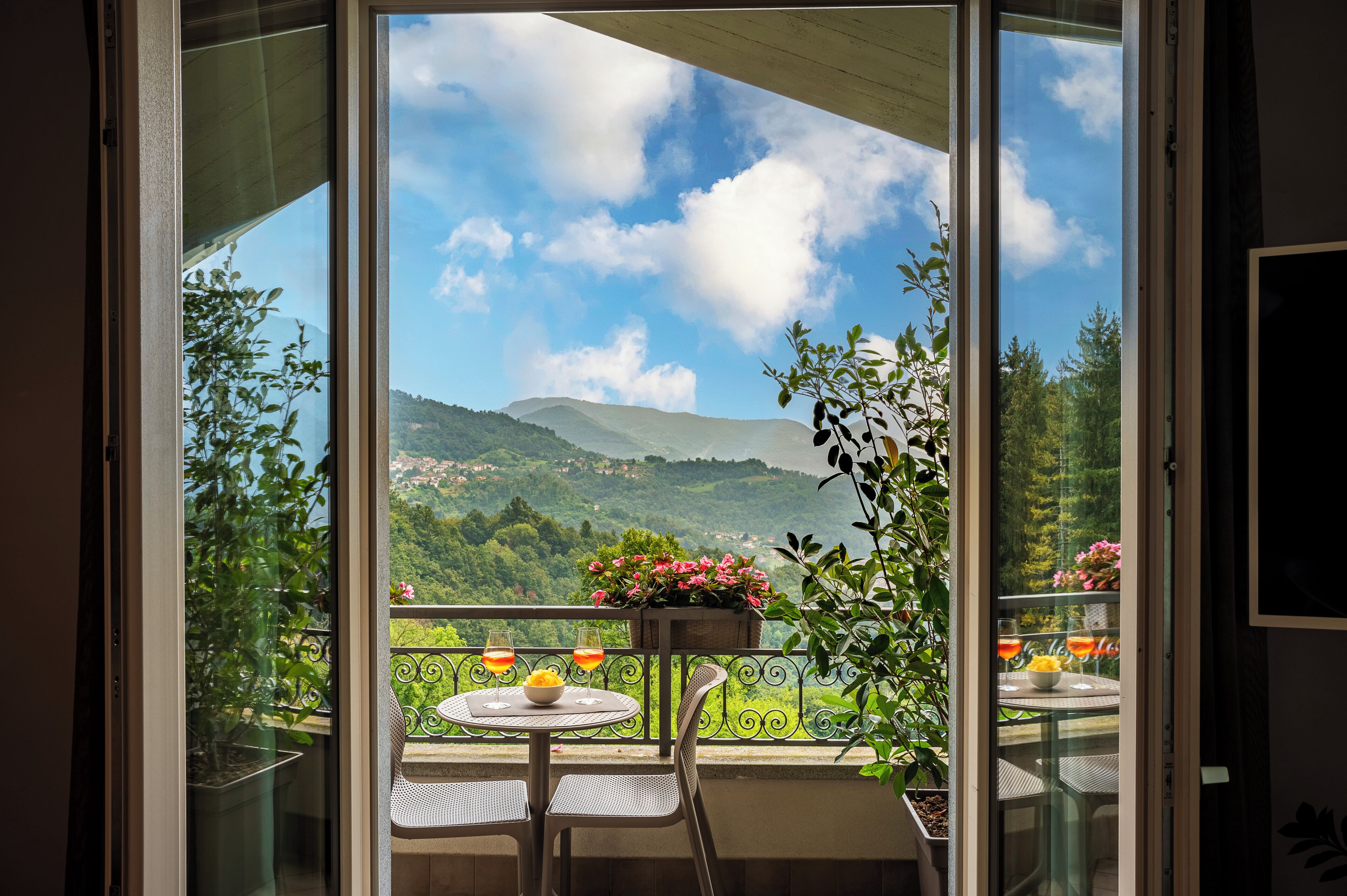 A balcony with a table and chairs, a potted plant, and a view of a mountainous landscape.