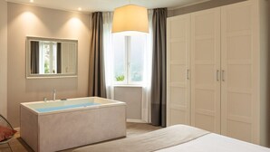 A modern bedroom with a large bed, a built-in bathtub, a mirror, and a wardrobe. - Rota Suites (Rota D'Imagna)
