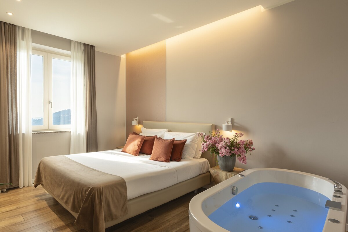 Ein Hotelzimmer mit einem Bett, einem großen Fenster, einer Whirlwanne und einer Blumenvase.