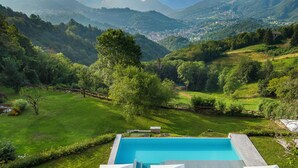 A swimming pool with lounge chairs and umbrellas, surrounded by a lush green landscape and mountains in the background. - Rota Suites (Rota D'Imagna)