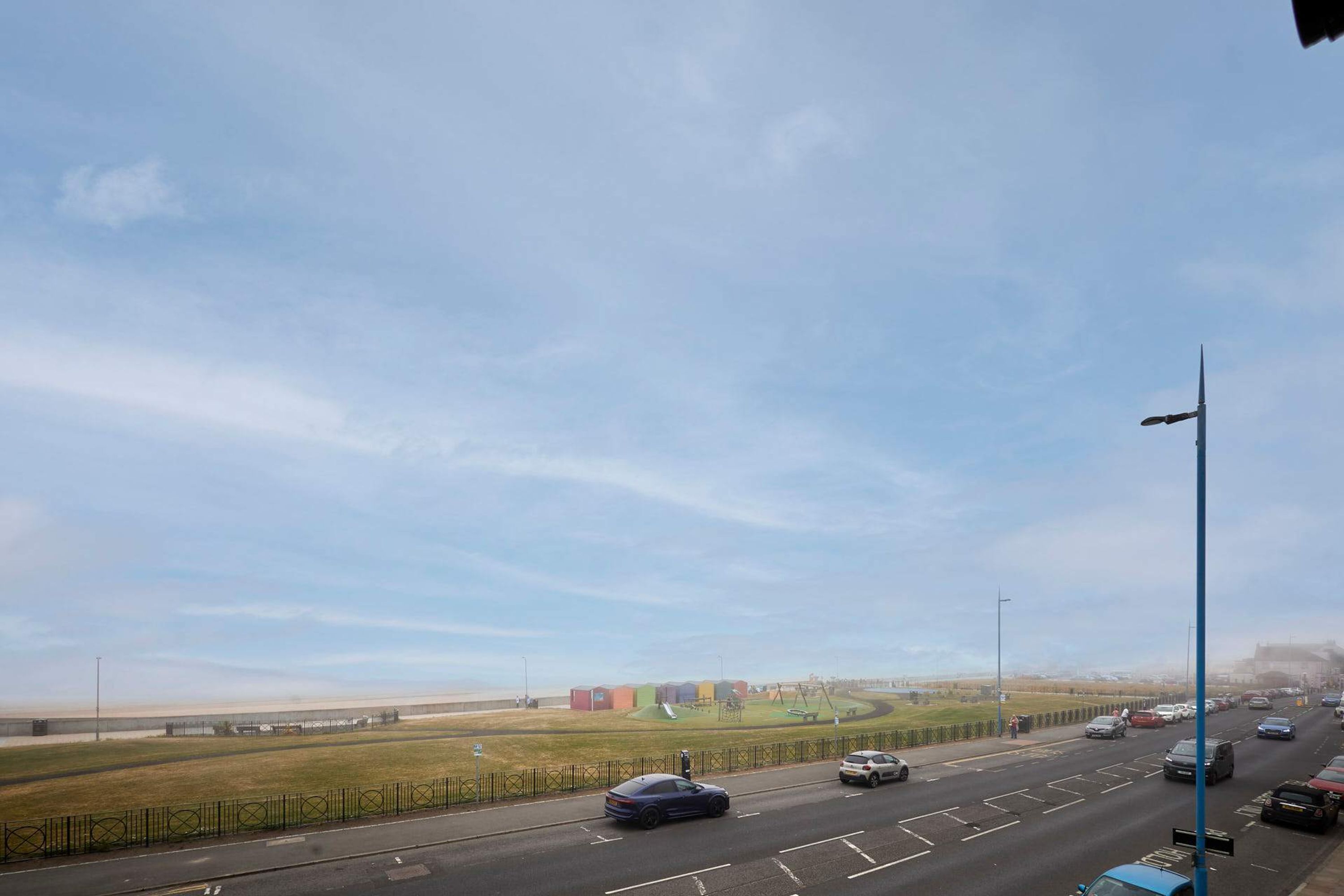 A multi-lane road with vehicles, a clear sky, and distant buildings.