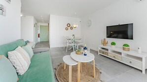 A modern living room with a green sofa, a white TV stand, and a dining area with a table and chairs. - Home Holidays 423 (CN)