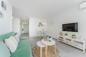 A modern living room with a green sofa, a white TV stand, and a dining area with a table and chairs. - Home Holidays 423 (CN)