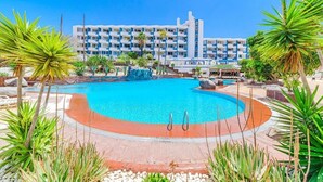 A hotel with a large swimming pool surrounded by tropical plants and a multi-story building with balconies. - Home Holidays 423 (CN)