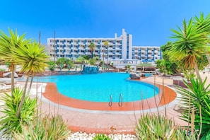 A hotel with a large swimming pool surrounded by tropical plants and a multi-story building with balconies. - Home Holidays 423 (CN)