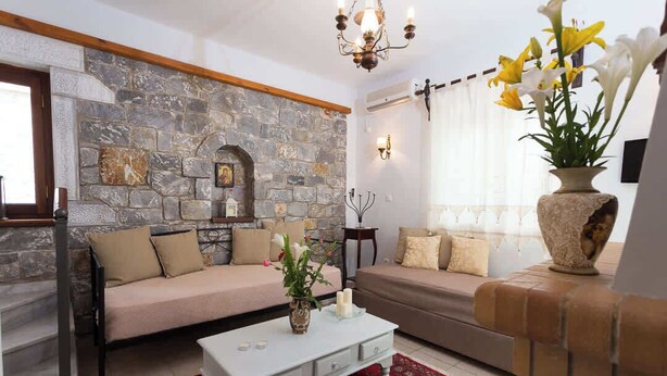 A living room with a stone wall, a sofa, a coffee table, and a vase with flowers. - Pleades Seaside Alcyone Gem in Mani Near the Sea (West Mani)