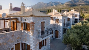 A stone building with a balcony, a mountain backdrop, and a clear sky. - Pleades Seaside Asterope Gem in Mani Near the Sea (West Mani)