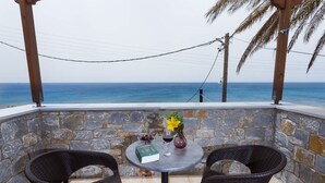 A stone-walled outdoor seating area with a table, two wicker chairs, a book, a vase with flowers, and a glass of wine. - Pleades Seaside Asterope Gem in Mani Near the Sea (West Mani)