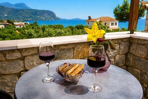Ein Tisch mit zwei Weingläsern und einer Schale mit Snacks, mit Blick auf eine Küstenlandschaft.