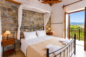 Ein Schlafzimmer mit Steinwand, einem Bett mit weißer Bettwäsche, einem Nachttisch mit Lampe und einem Balkon mit Blick.