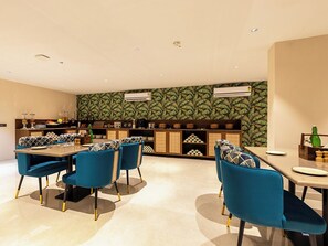 Uma sala de jantar moderna com cadeiras azuis, uma mesa de madeira e uma cozinha ao fundo.