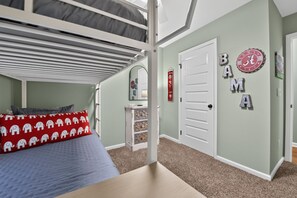 A bunk bed with a red pillow, a dresser, a mirror, and a wall with 'BAMMA' letters and a clock.