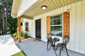 A house with a covered porch, a black door, and two metal chairs.