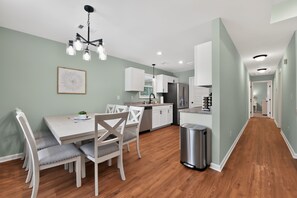 A modern kitchen with white cabinets, a stainless steel refrigerator, and a dining area with a table and chairs.