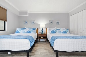 A bedroom with two beds, a nightstand, a lamp, and artwork on the walls. - Beach Colony Oceanfront 3BR Corner Retreat (Myrtle Beach)
