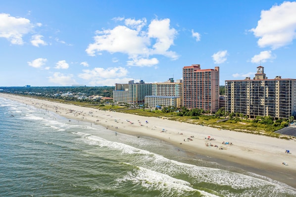 Ein Strandhotel mit mehreren Hochhäusern, einem Sandstrand und Wellen.