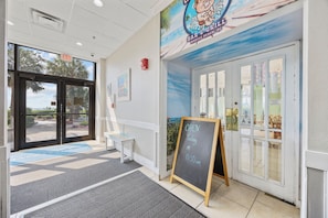 A bar entrance with a chalkboard sign indicating it's open, a bench, and a door leading outside. - Beach Colony Oceanfront 3BR Corner Retreat (Myrtle Beach)