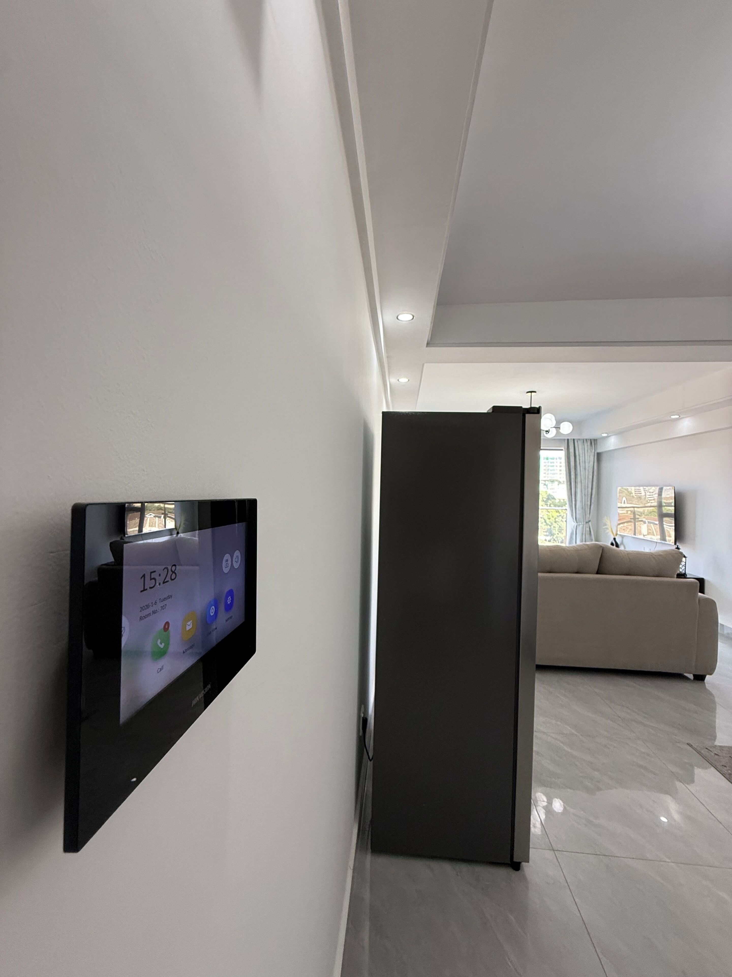 Una sala de estar moderna con una televisión de pantalla plana montada en la pared, un mueble de color oscuro y un sofá color beige.
