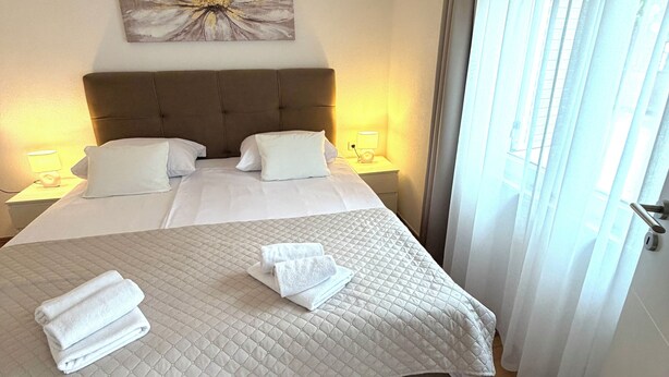 Quarto de hotel com uma cama, duas luminárias de cabeceira, uma obra de arte na parede e uma janela com cortinas.