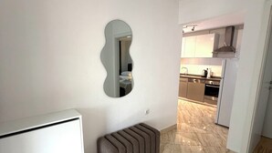 Quarto com radiador branco, um banco, um espelho e uma área de cozinha ao fundo.