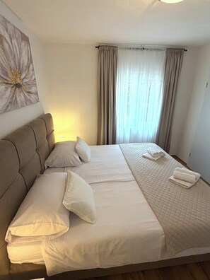 Ein Hotelzimmer mit einem großen Bett, einem Kopfteil, einem Wandbild und einem Fenster mit Vorhängen.