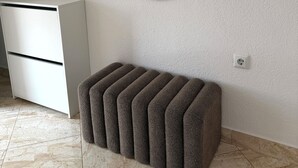 Quarto com penteadeira branca, um banquinho marrom, espelho fixado na parede e piso ladrilhado.