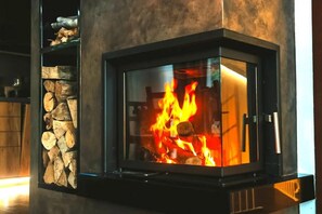 A fireplace with a glass front, logs stacked to the left, and a metal handle on the right.