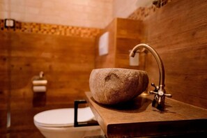 A bathroom with a stone sink, a wooden vanity, and a toilet.