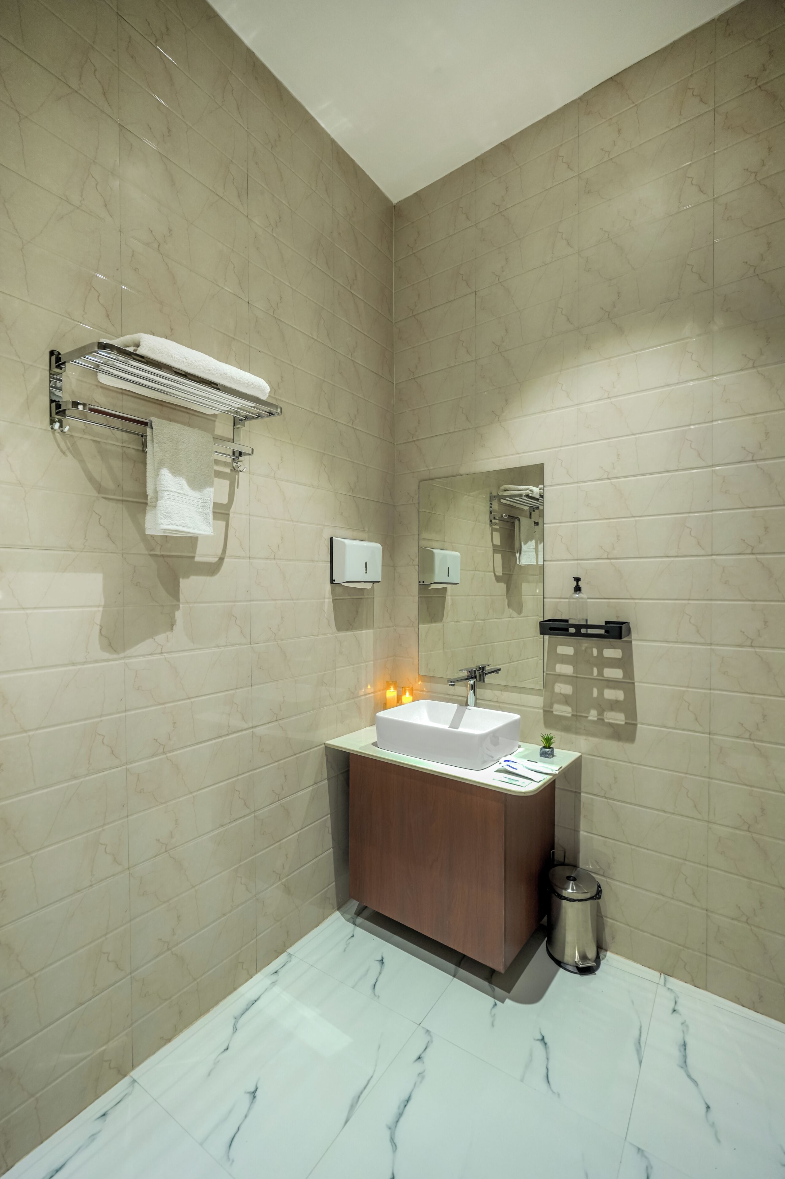 A modern bathroom with a marble-tiled wall, a white sink, a mirror, a towel rack, and a trash bin.