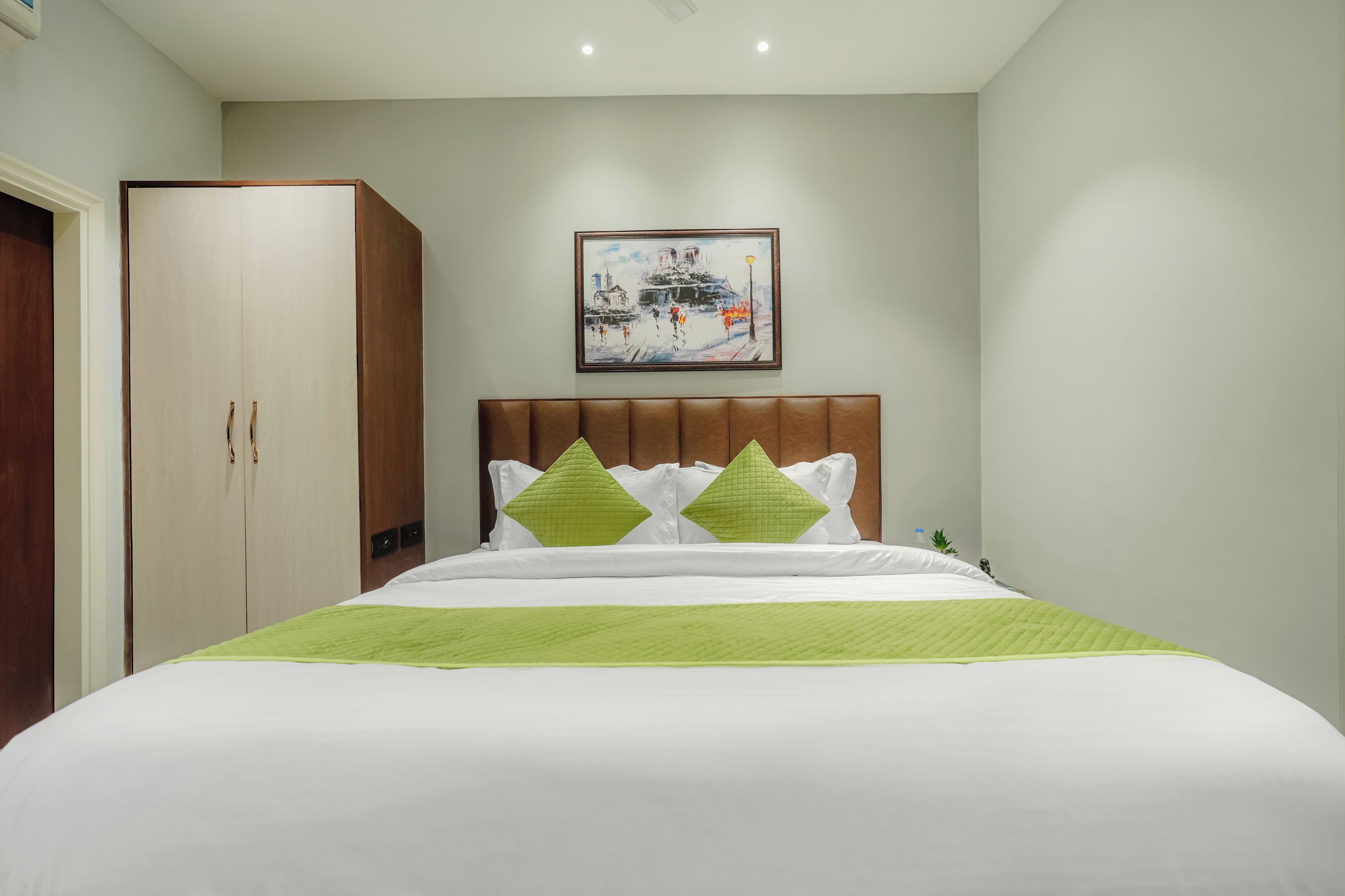 A hotel room with a bed, a wardrobe, a painting on the wall, and a green bedspread.