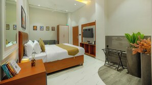 A modern bedroom with a bed, bedside table, books, a TV, a wardrobe, and a plant.